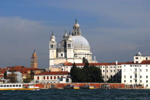La basilica barocca di Santa Maria della Salute, dall’isola della Giudecca a Fondamenta Zitelle, eretta nell'area della Punta della Dogana, nel sestiere di Dorsoduro. A sinistra Il campanile della chiesa di Santo Stefano, di impianto romanico con cella a tre archi e sovrastato da un tamburo ottagonale, caratterizzato da un'accentuata pendenza.
