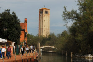 La Strada della Rosina: è la strada principale che unisce lo scalo del vaporetto con la Piazza di Torcello. Sullo sfondo il campanile della Basilica di Santa Maria Assunta una volta cattedrale della soppressa diocesi di Torcello. In basso il ponte del Diavolo privo di parapetti.